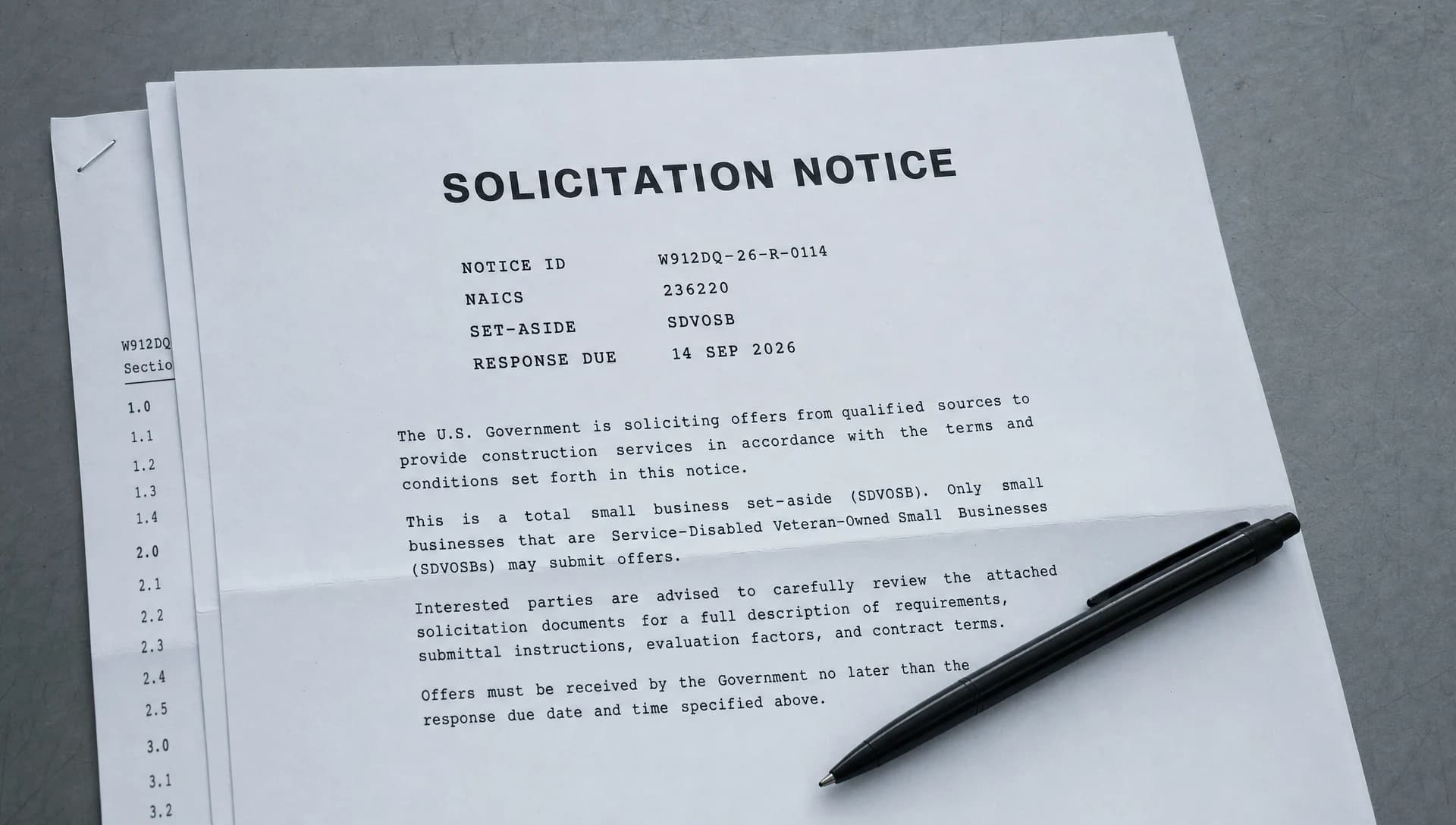 A printed federal solicitation notice showing notice ID, NAICS code, set-aside and response date, lying on a grey steel desk on top of a stack of further printed solicitation pages, with a pen resting across the lower corner
